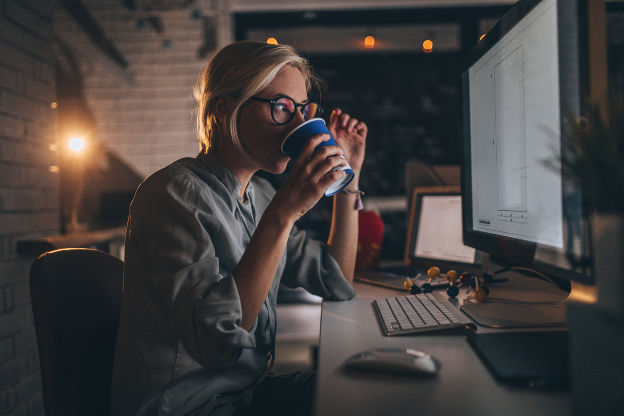 A woman drinking coffee in front of a computer late at night.