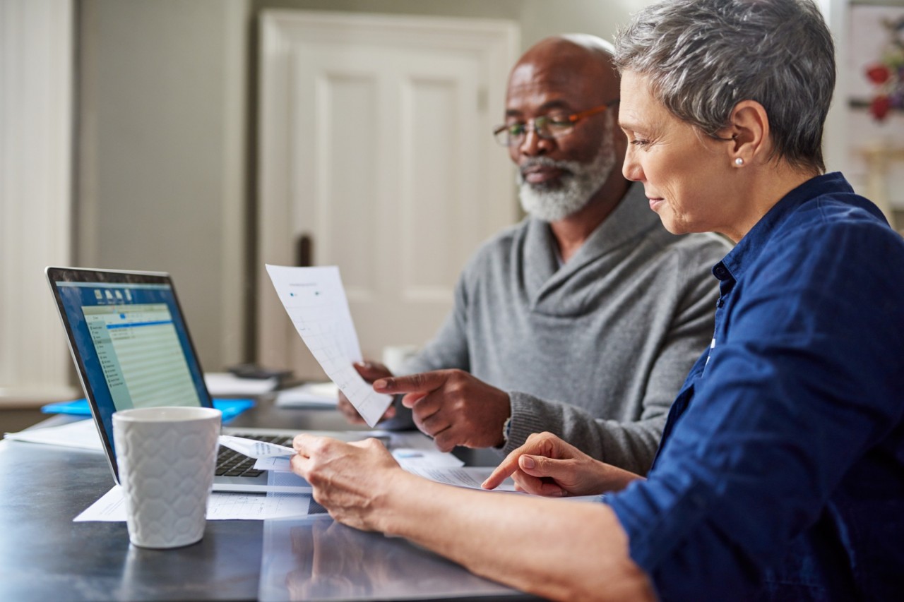 An older couple sitting at a table looking at a laptop and notes discussing their financial future.