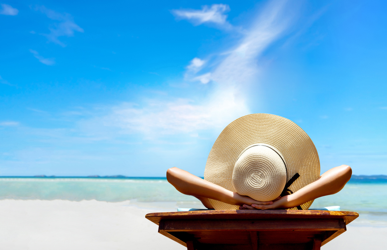 A woman laying on the beach in a sun hat on a sunny day.