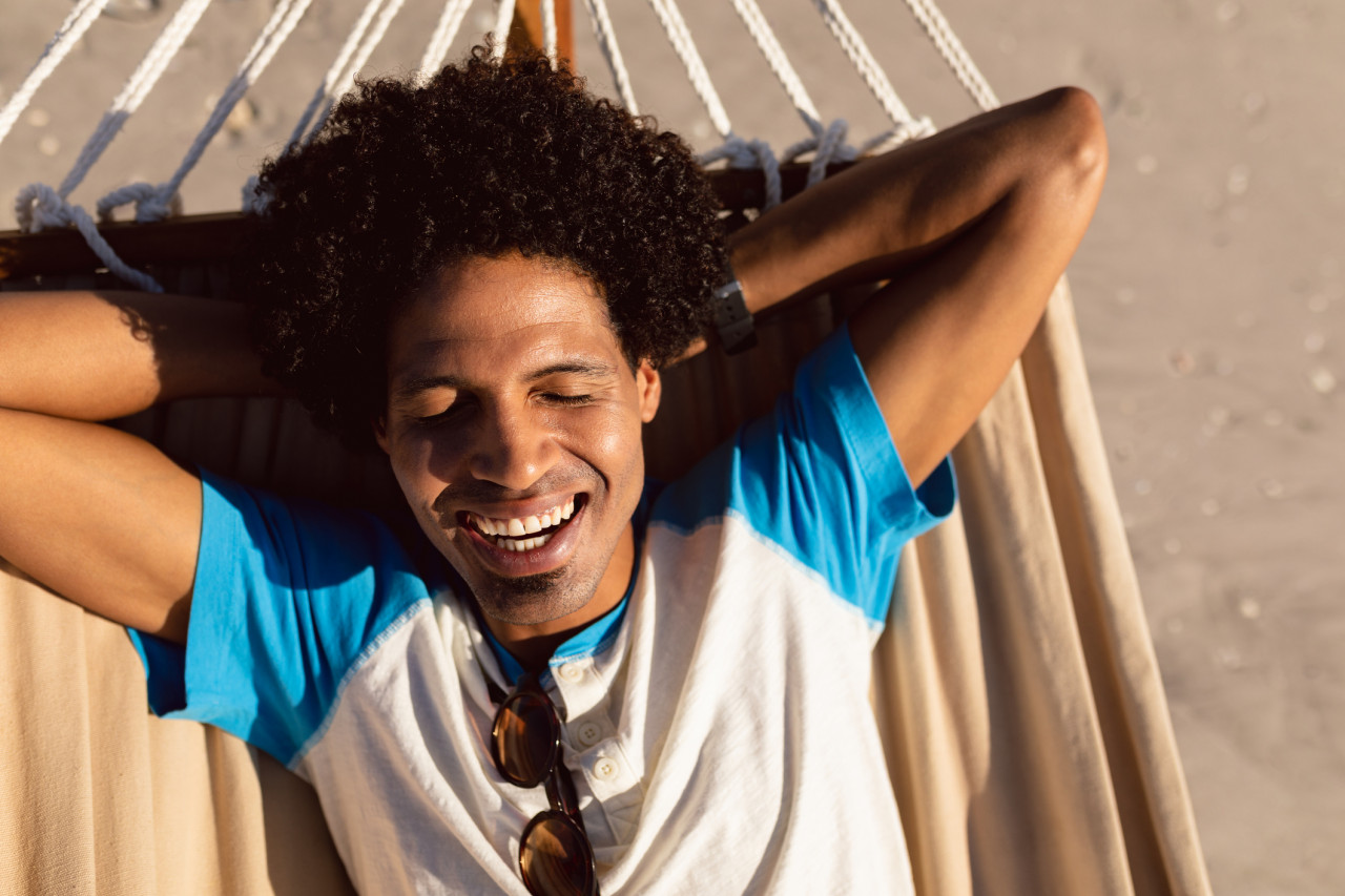 Happy young man laying in hammock on the beach with sun shining.
