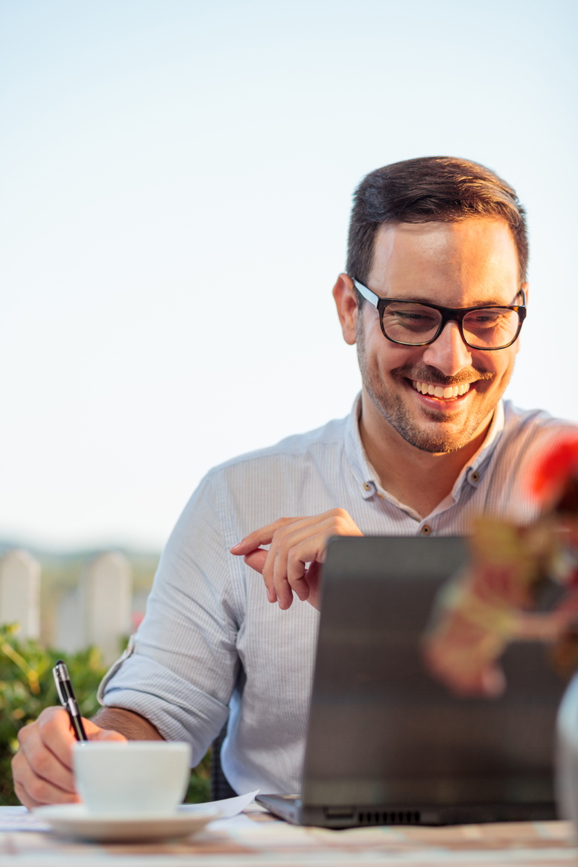 A happy young businessman working on his computer outside.