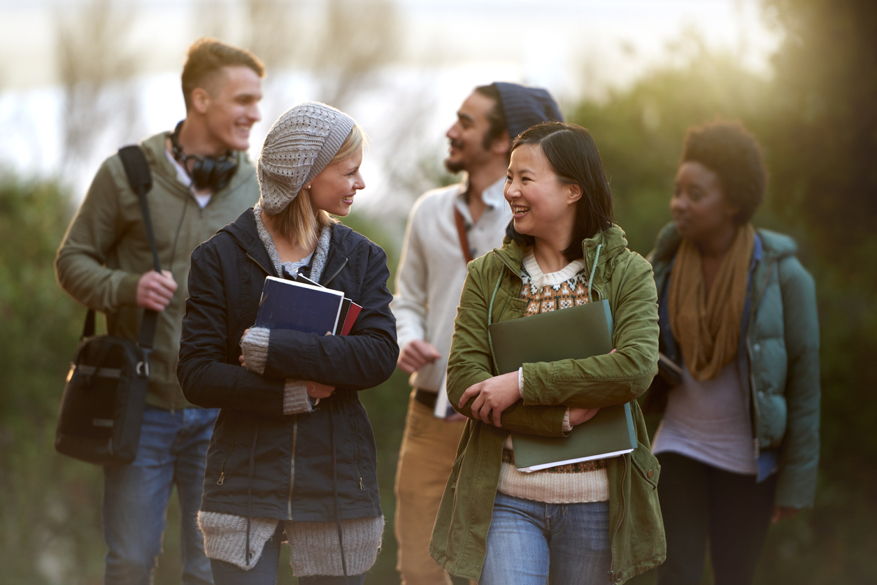 A group of students carrying books and having a conversation while walking outside.