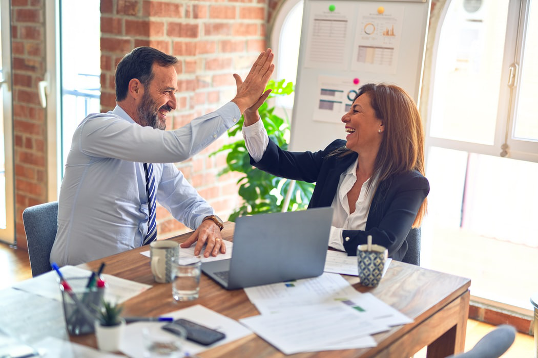 A man and woman high-fiving at a table with a laptop and documents sitting on it.