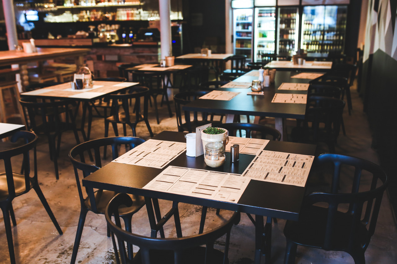 An empty restaurant with tables and chairs set with menus.
