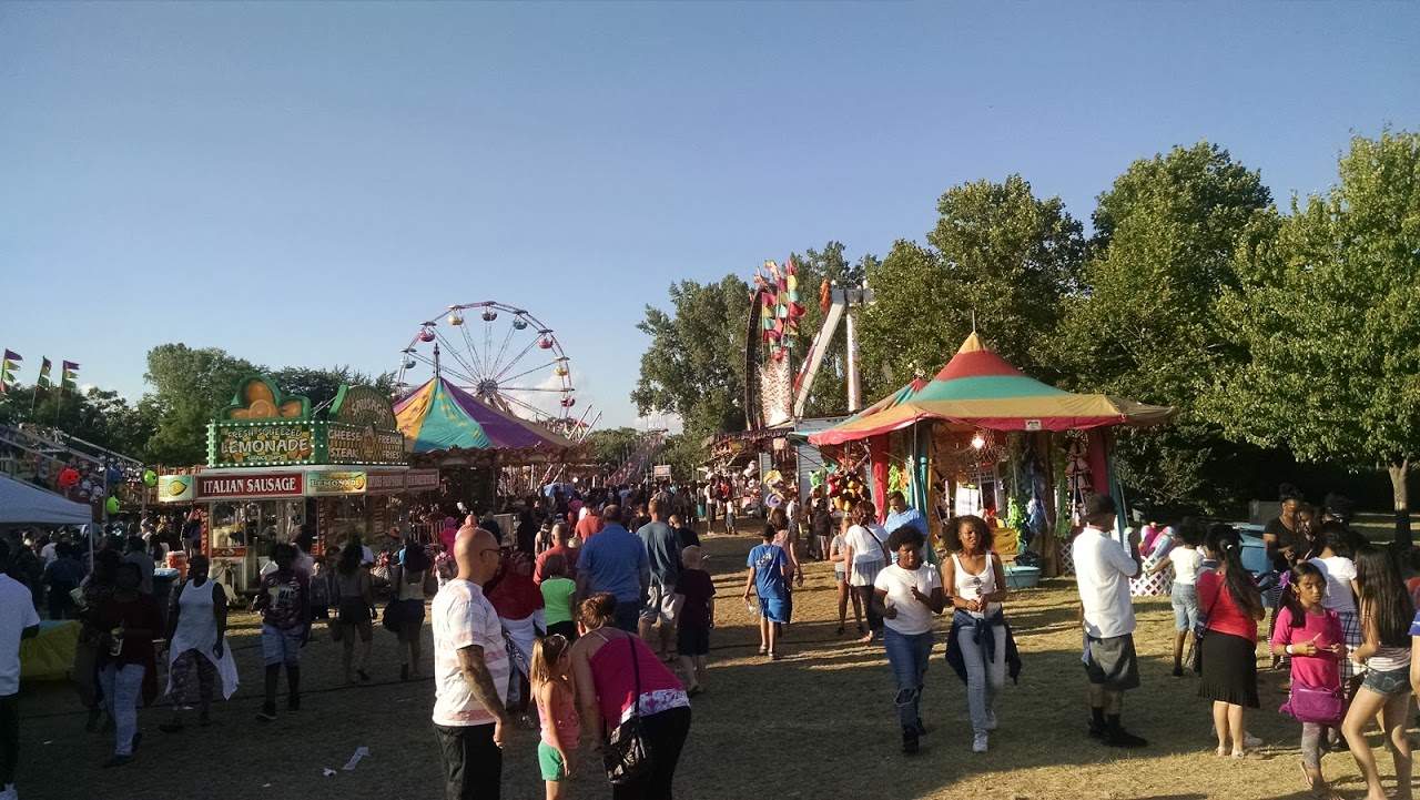 A crowd at a festival with a ferris wheel off in the distance.