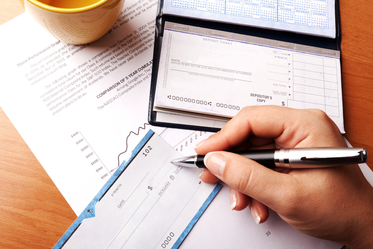Atop a table is a checkbook and a woman's hand filling out a check for a utility bill.