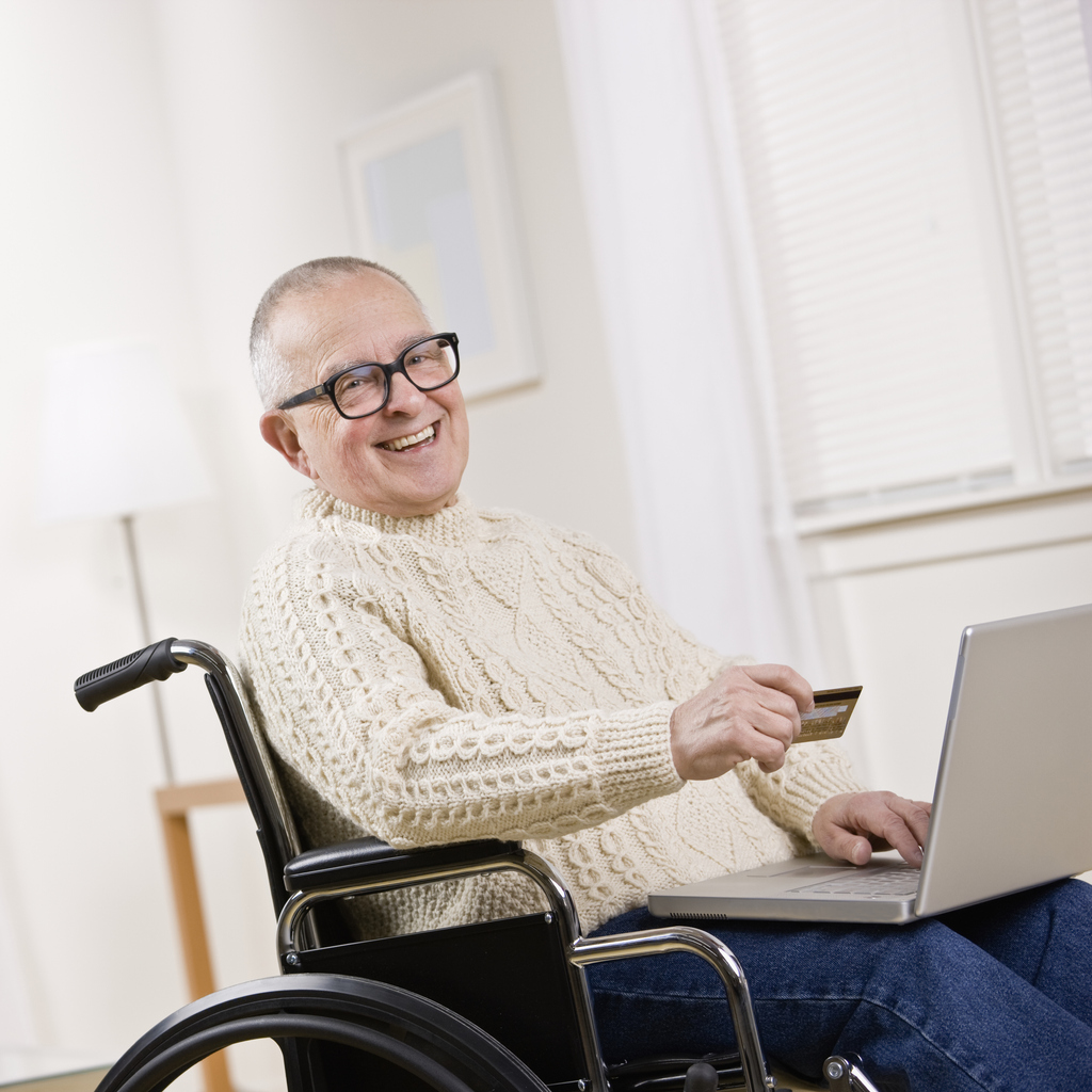 A man smiling in a wheelchair with a laptop and credit card.