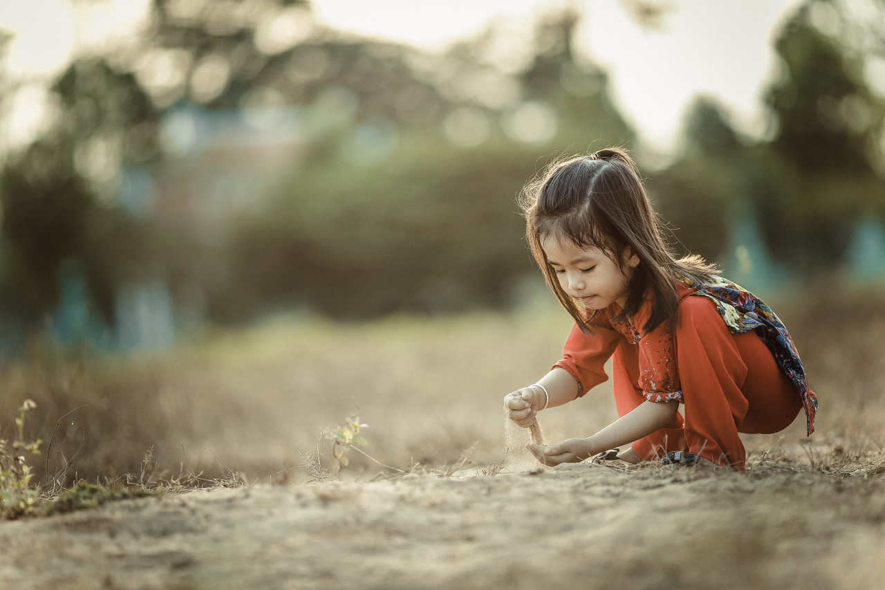 A child squatting down outside and playing with sand.